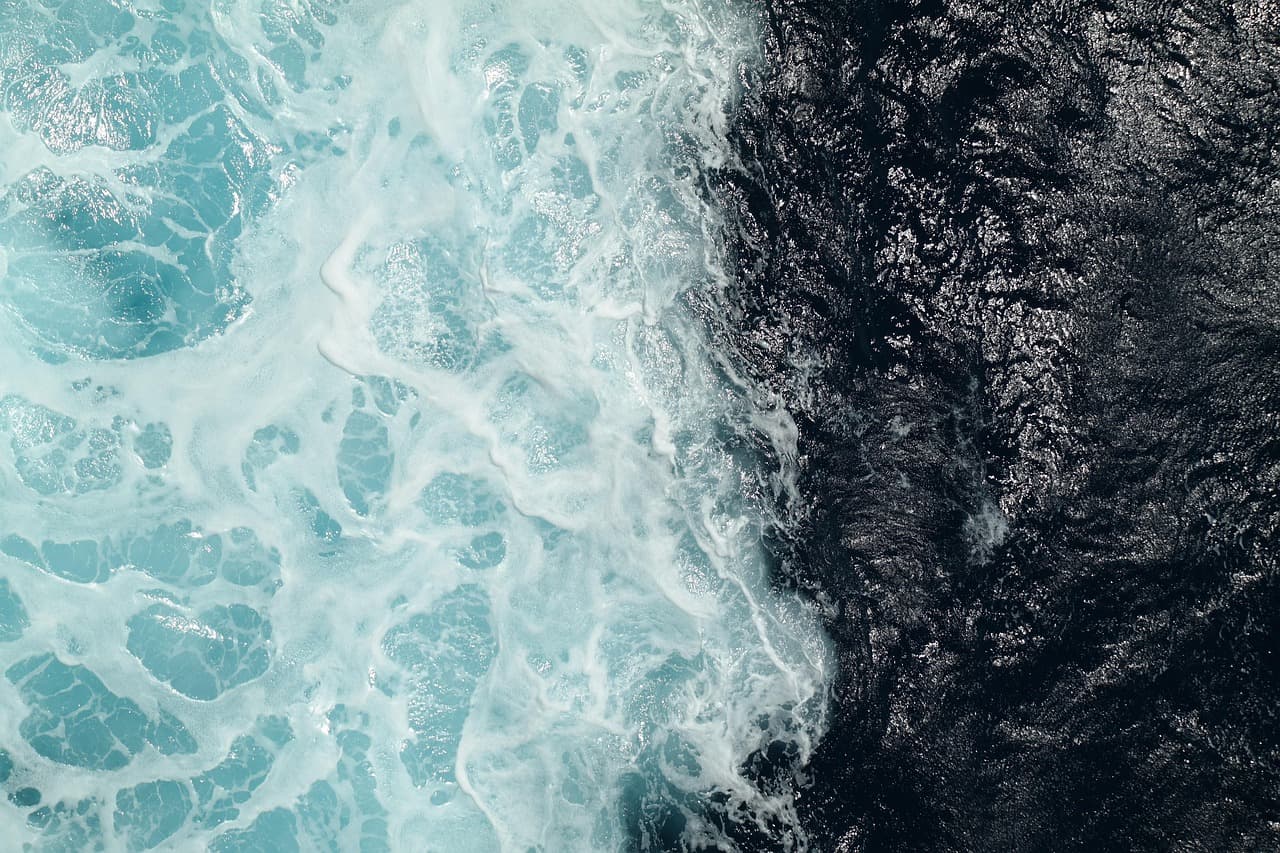 Aerial view of turquoise sea foam meeting dark coastal water