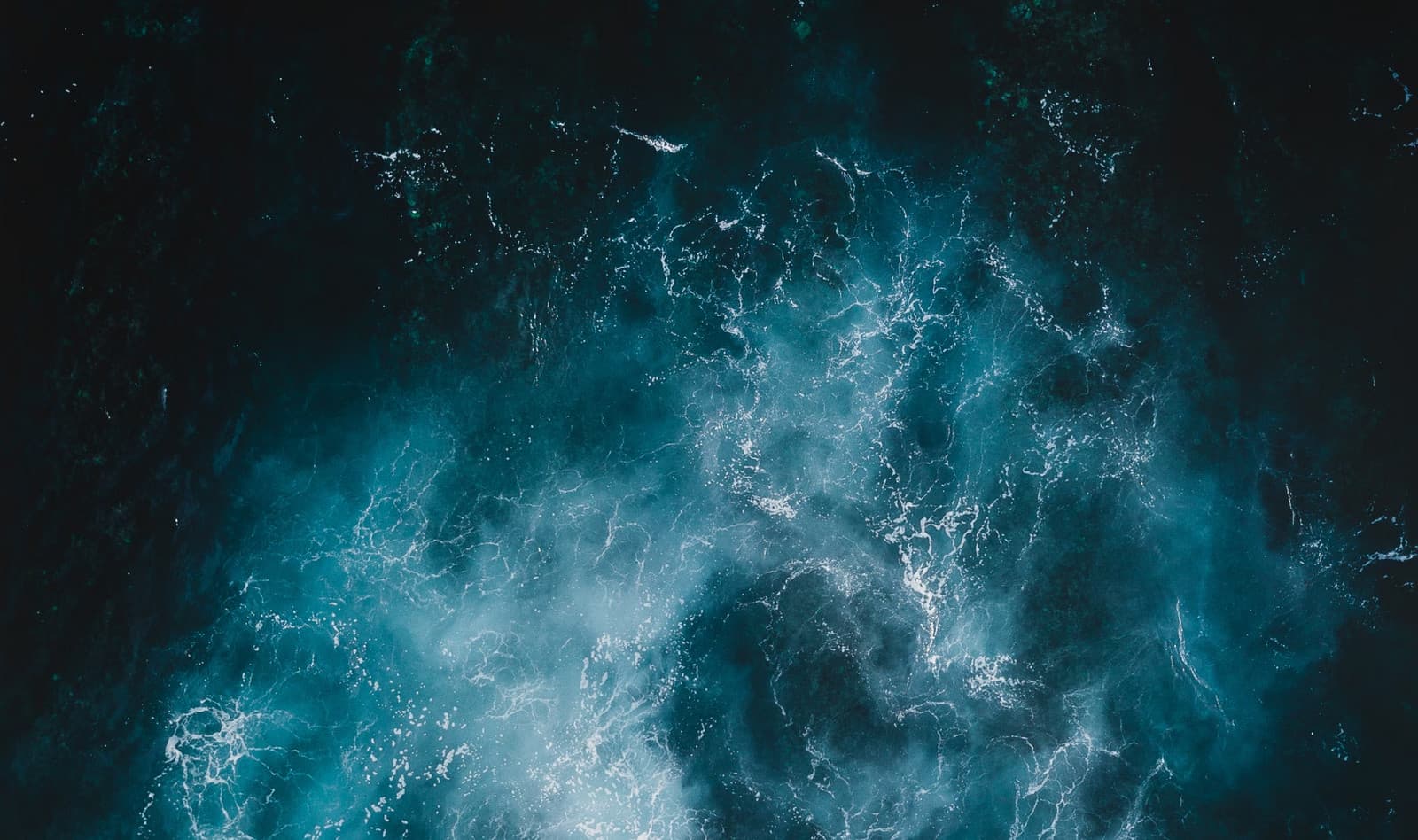 Aerial view of deep blue ocean water with white foam swirls